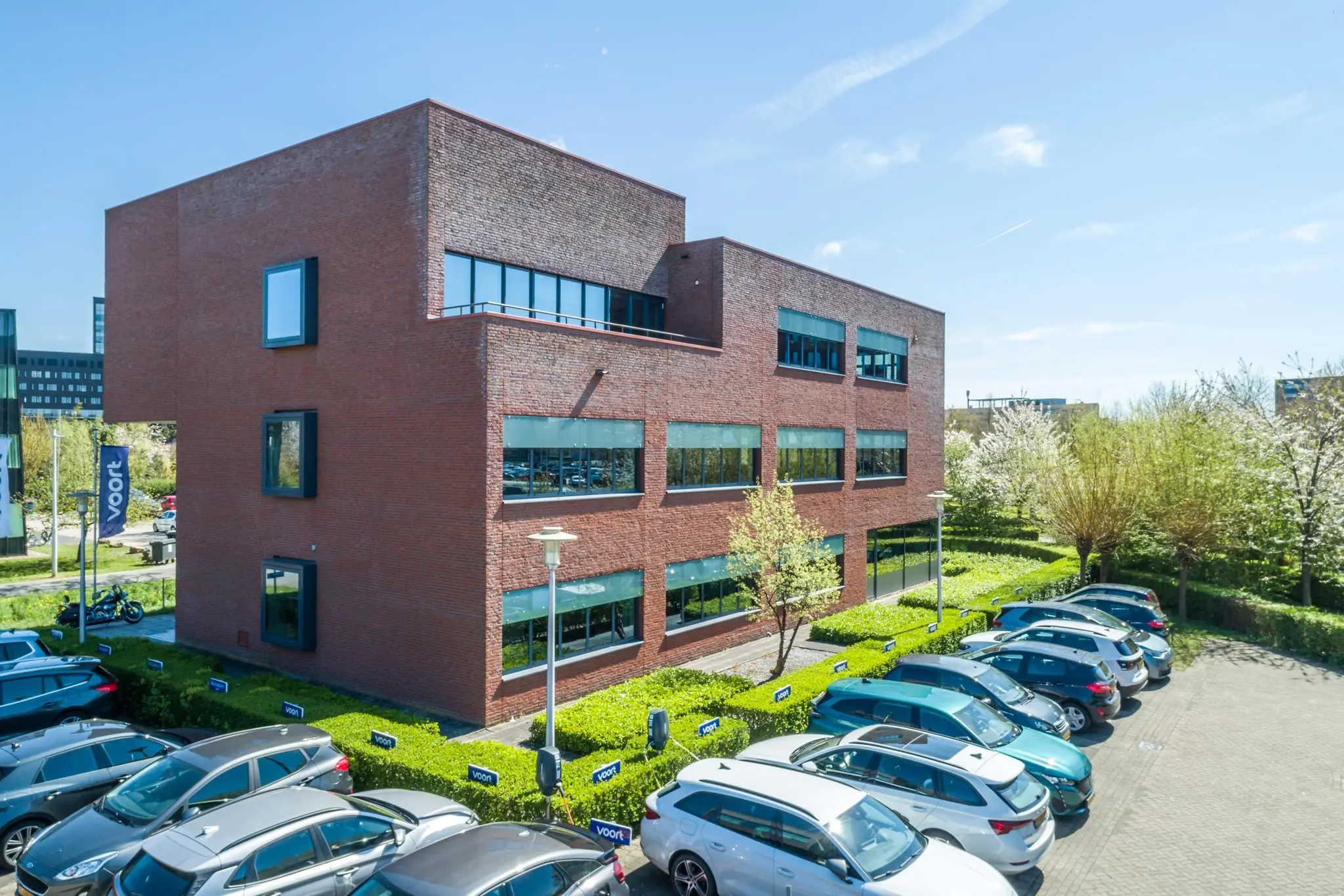 Modern kantoorgebouw aan de Groenewoudsedijk met parkeerplaatsen en omliggend groen.