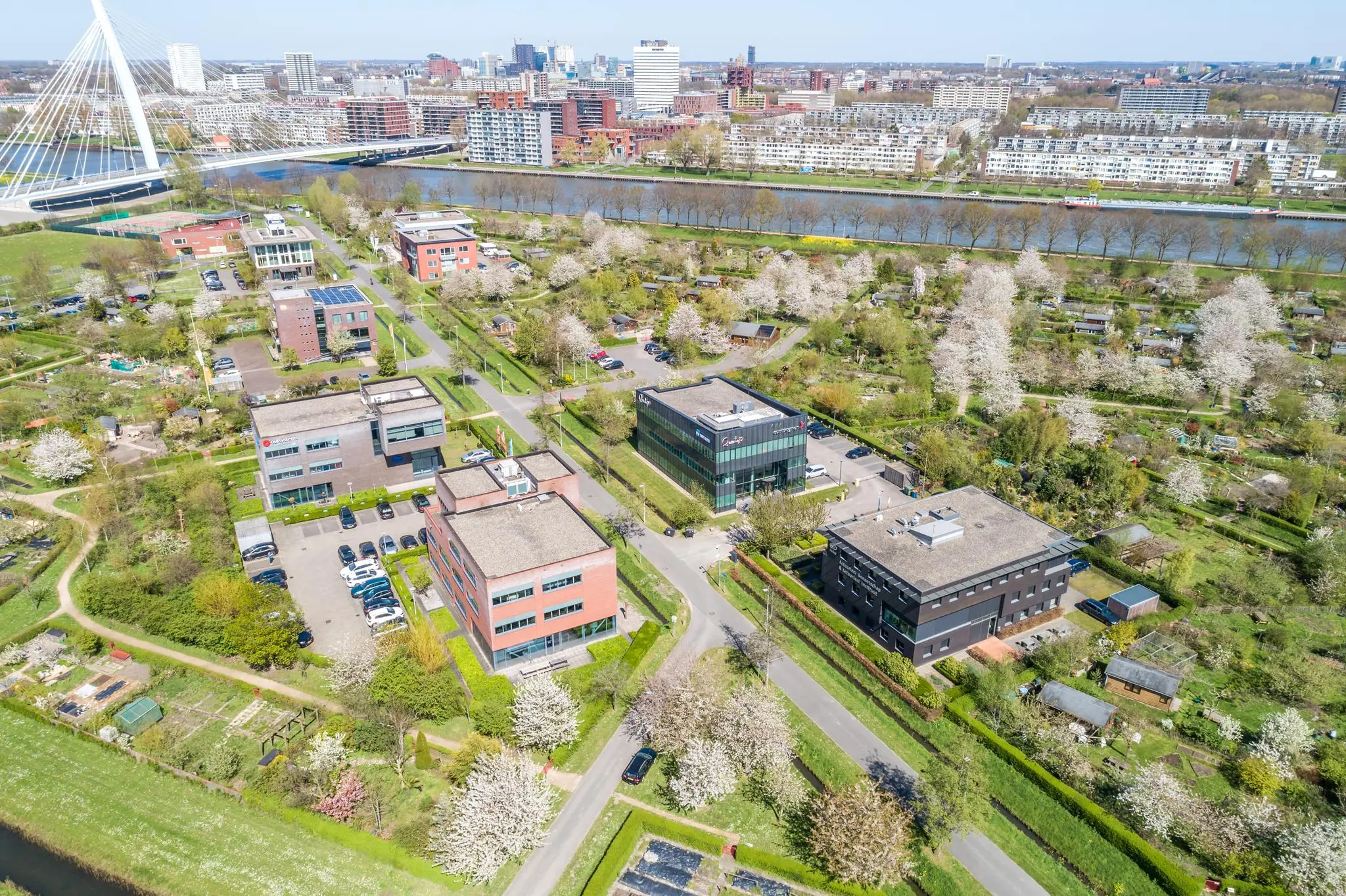 Luchtfoto van kantoren aan de Groenewoudsedijk in Utrecht, omringd door bloeiende volkstuinen en met uitzicht op de stad en het Amsterdam-Rijnkanaal.