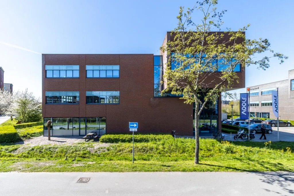 Modern kantoorpand aan de Groenewoudsedijk met bakstenen gevel, grote ramen en een parkeerterrein met vlaggen van bedrijf 4Dot.