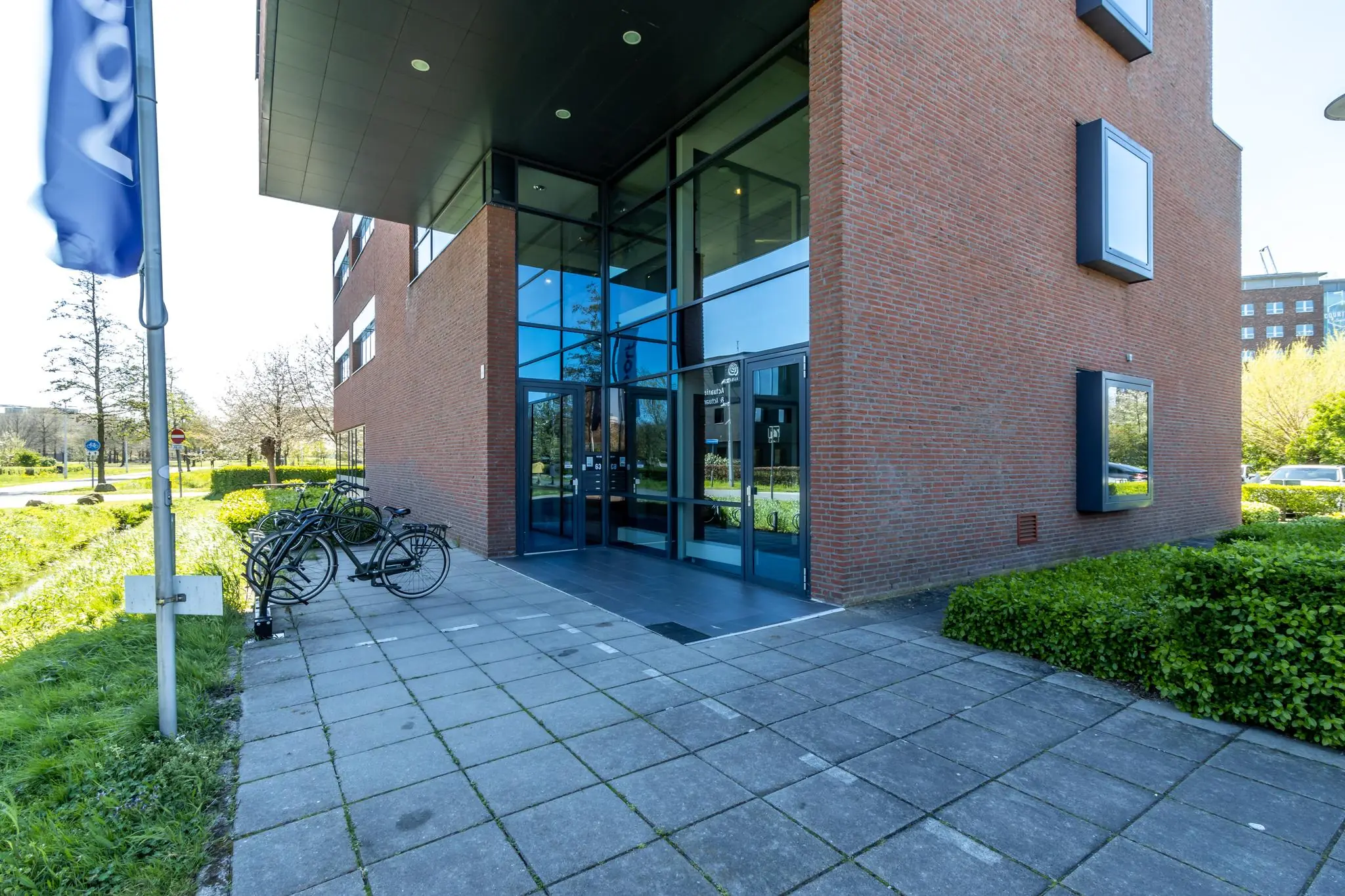 Ingang van een modern kantoorgebouw aan de Groenewoudsedijk met fietsenrek en glazen entree.