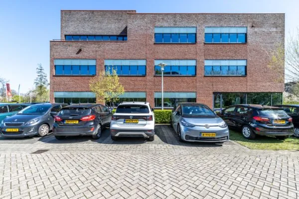 Parkeerplaats met geparkeerde auto's voor een modern kantoorgebouw aan de Groenewoudsedijk.