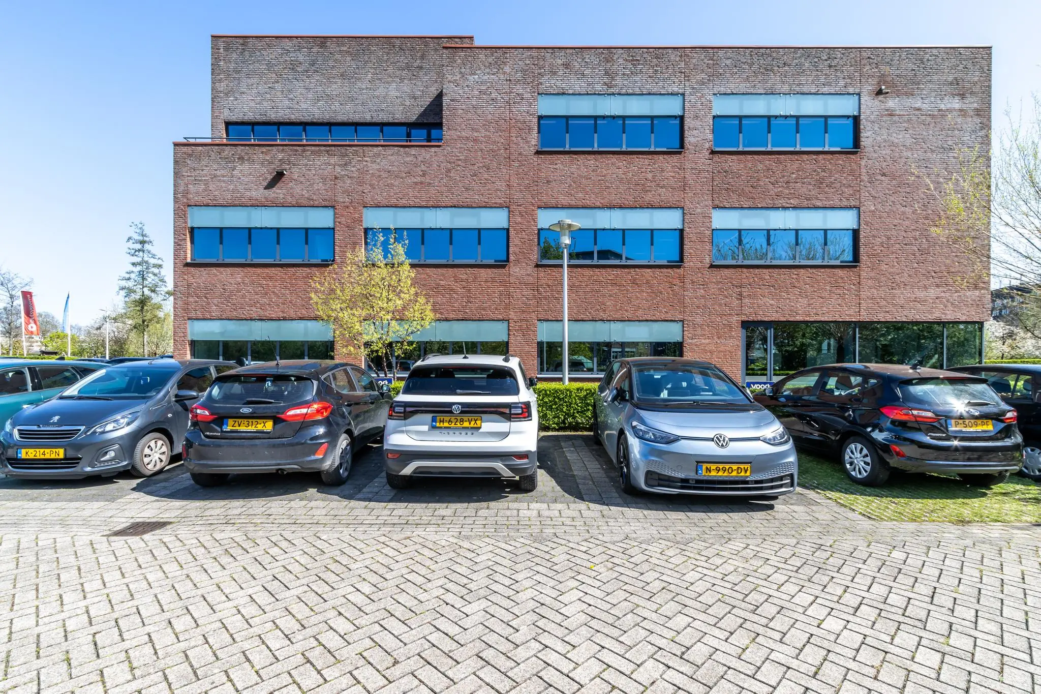 Parkeerplaats met geparkeerde auto's voor een modern kantoorgebouw aan de Groenewoudsedijk.
