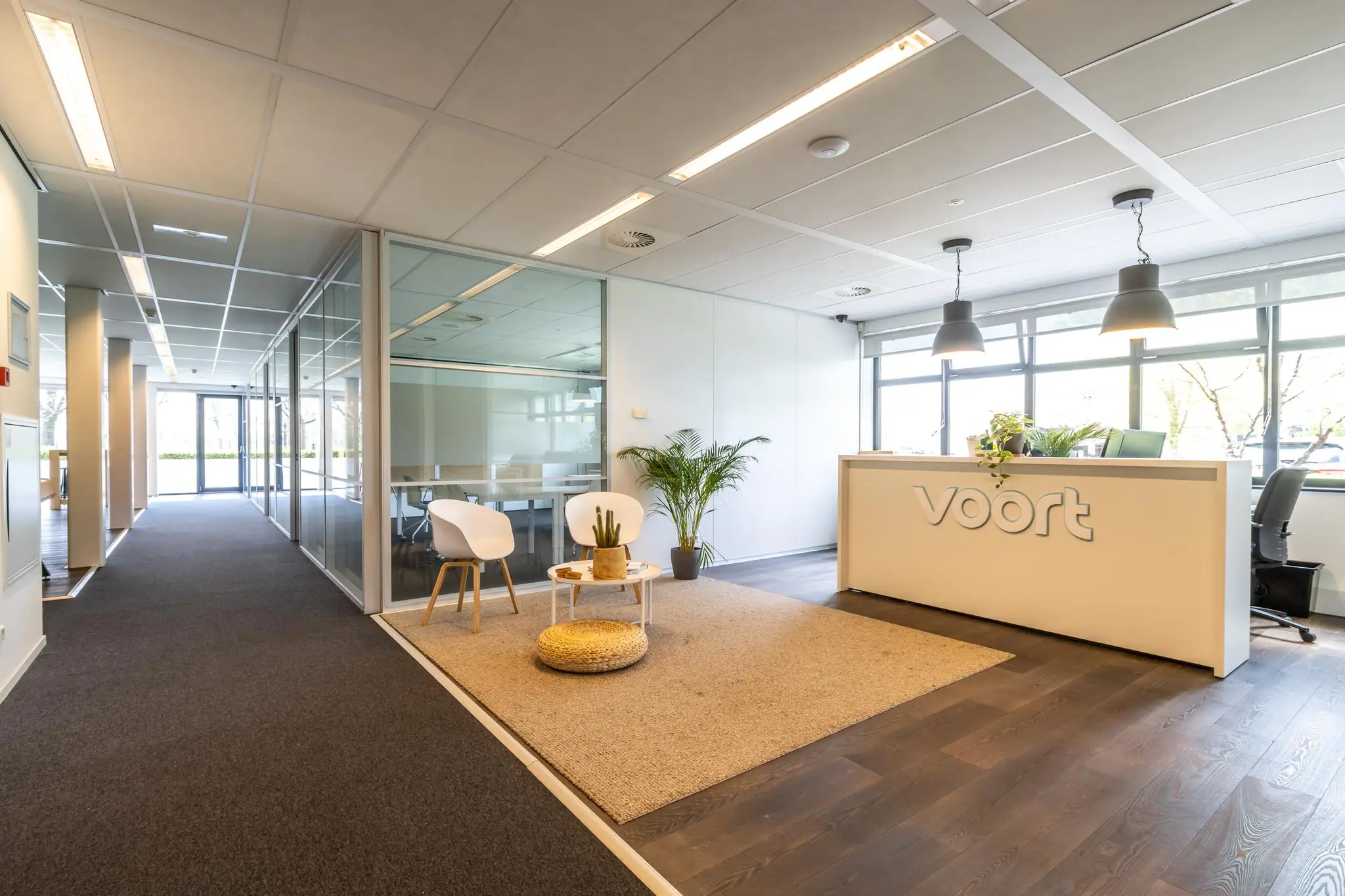 Moderne en lichte receptieruimte van kantoor Voort aan de Groenewoudsedijk, met balie, zithoek en glazen vergaderruimtes.