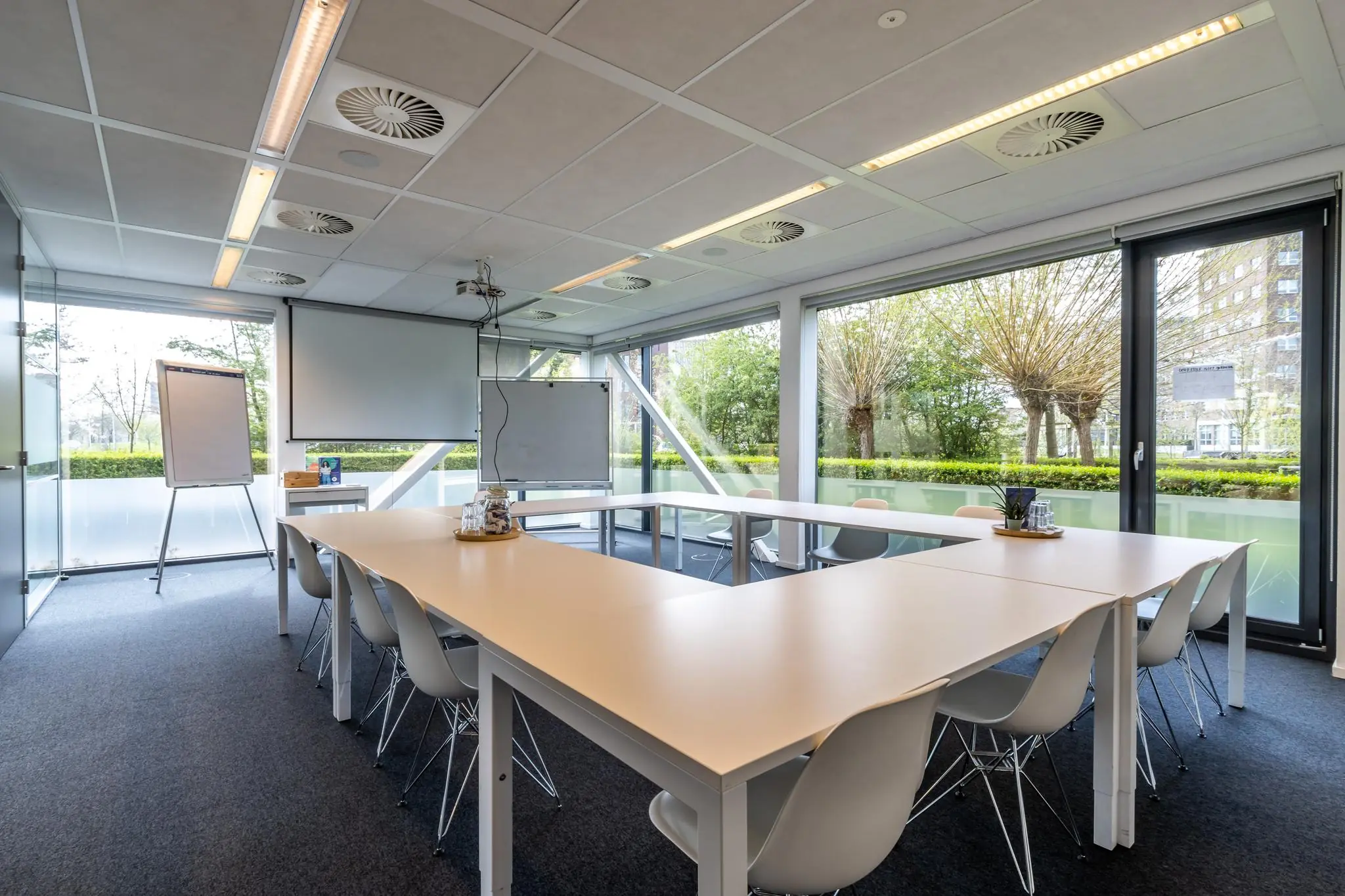 Moderne vergaderruimte aan de Groenewoudsedijk met U-vormige tafelopstelling, grote ramen en uitzicht op groen.