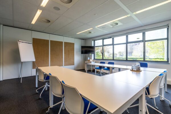 Vergaderruimte aan de Groenewoudsedijk met moderne inrichting, een flip-over, groot raam en flatscreen.