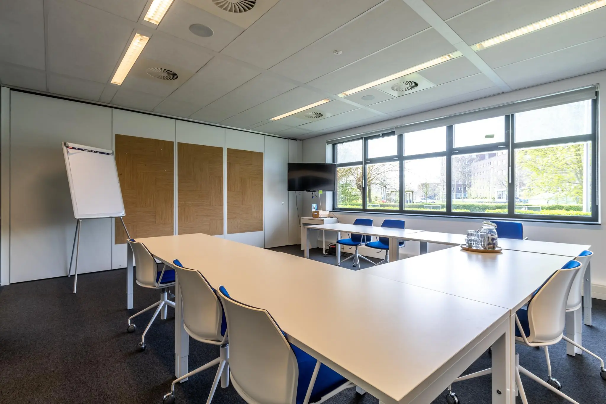Vergaderruimte aan de Groenewoudsedijk met moderne inrichting, een flip-over, groot raam en flatscreen.
