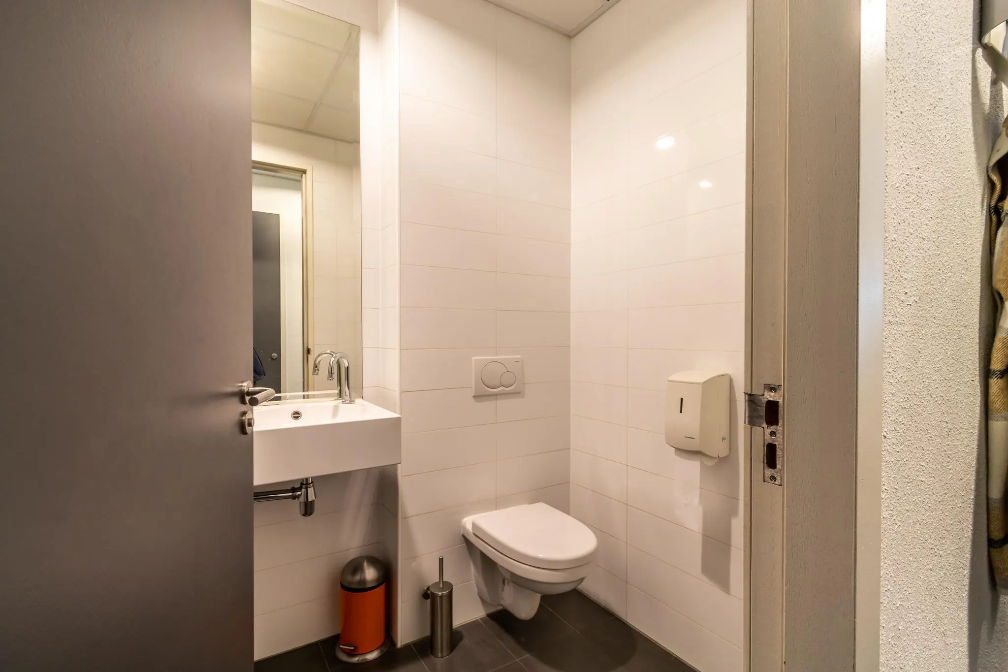 Moderne, strak afgewerkte toiletruimte met wandcloset, fontein en spiegel aan de Groenewoudsedijk.