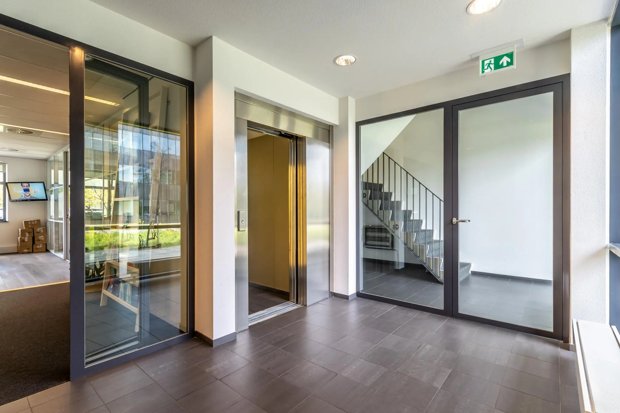 Moderne entree met een open liftdeur, glazen deuren en een trapopgang in een kantoorgebouw aan de Groenewoudsedijk.