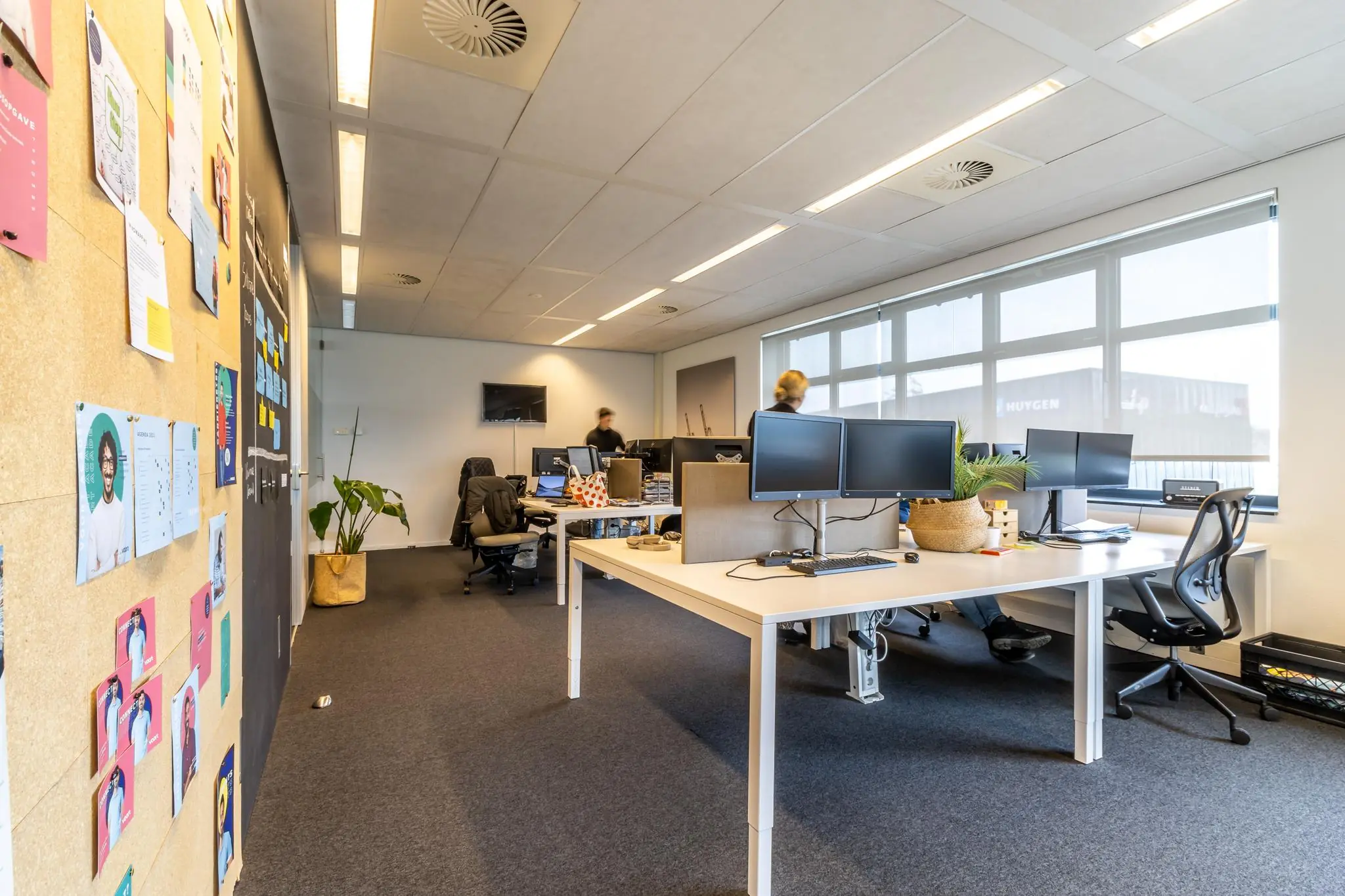 Modern kantoorinterieur aan de Groenewoudsedijk met werkplekken, computers en een prikbord met kleurrijke kaarten.
