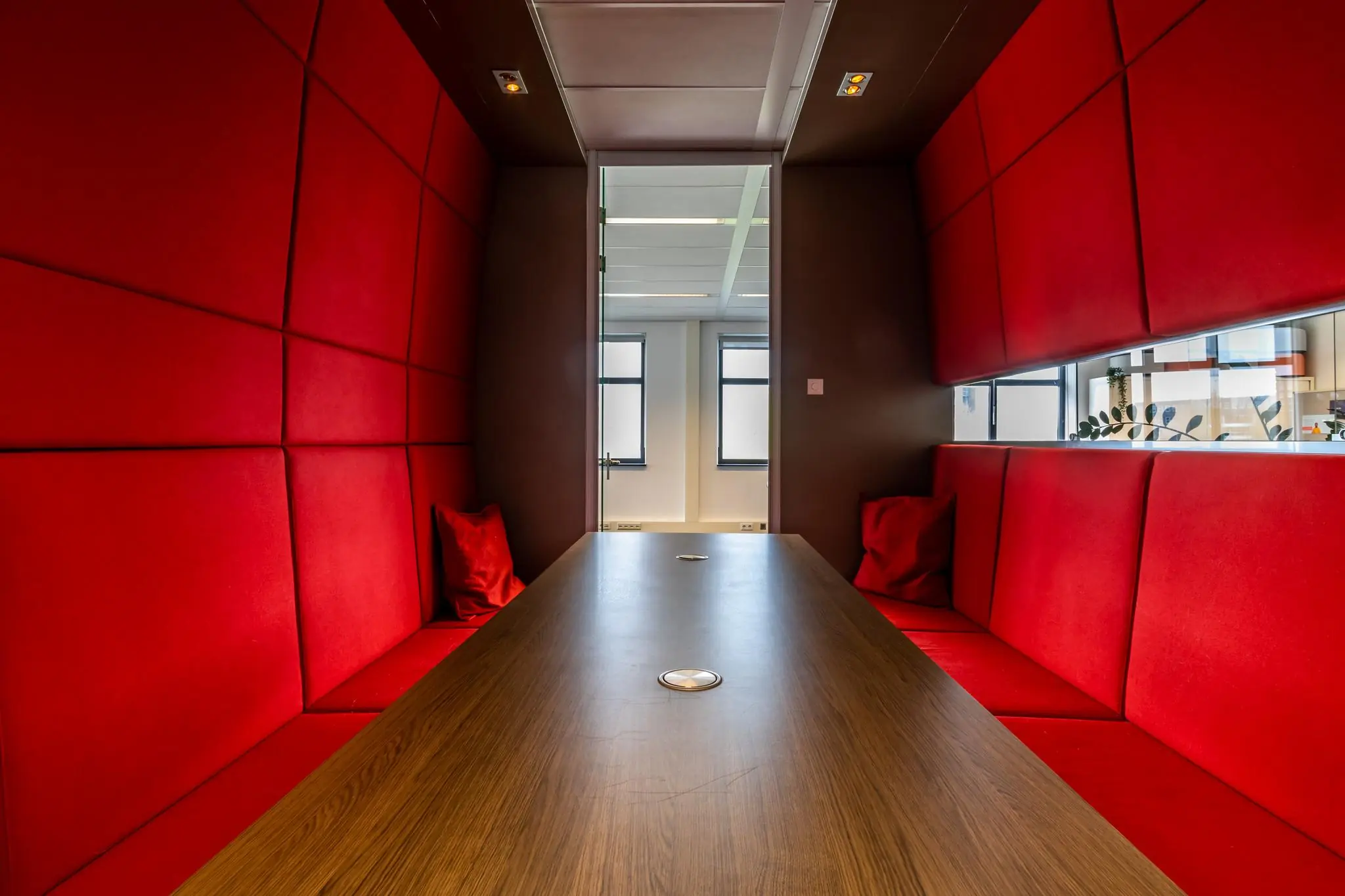 Moderne vergaderruimte aan de Groenewoudsedijk met rode zitbanken en een houten tafel.