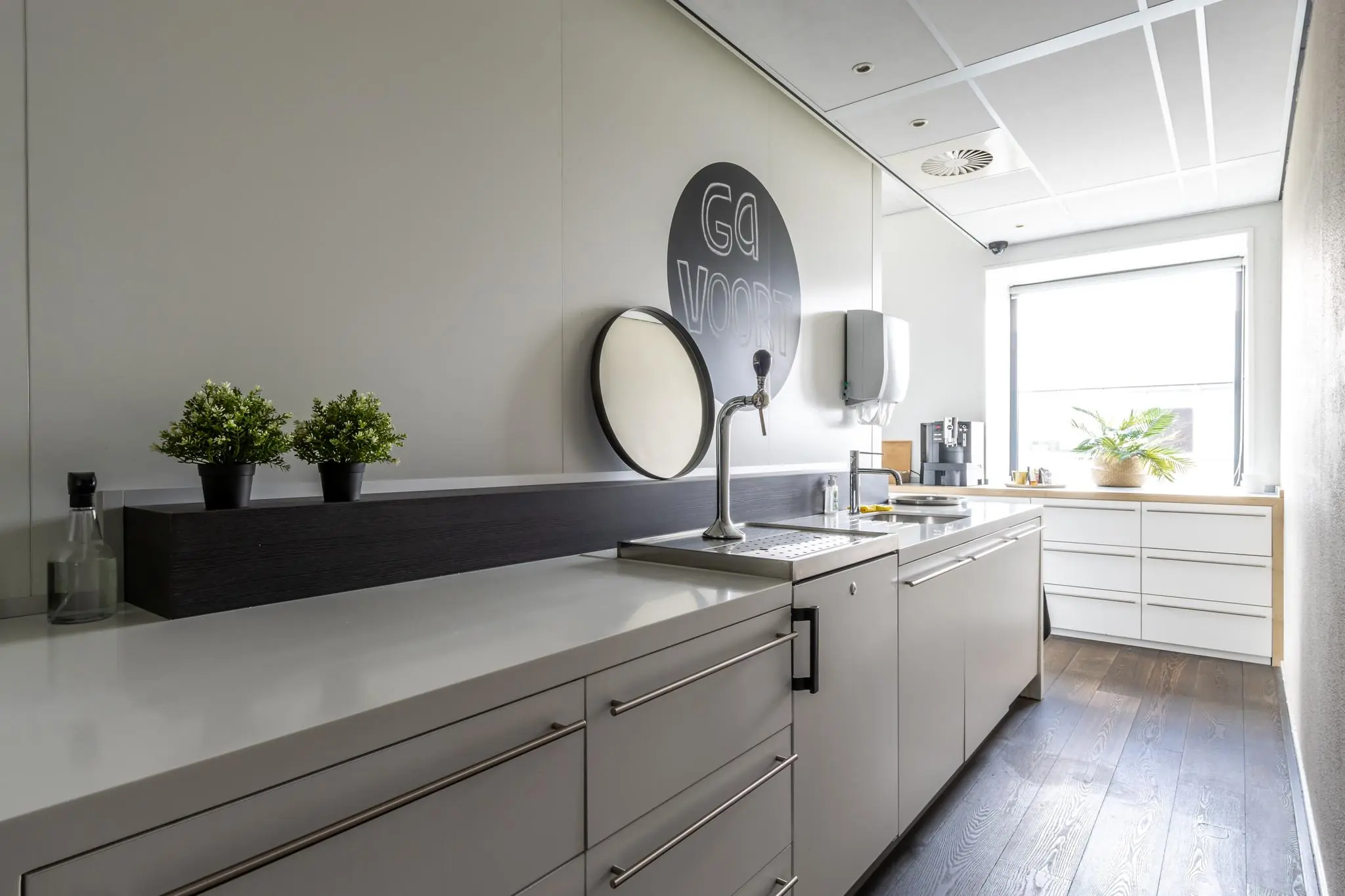 Moderne pantry met strakke kasten, een tapkraan, koffiemachine en planten, gelegen aan de Groenewoudsedijk.