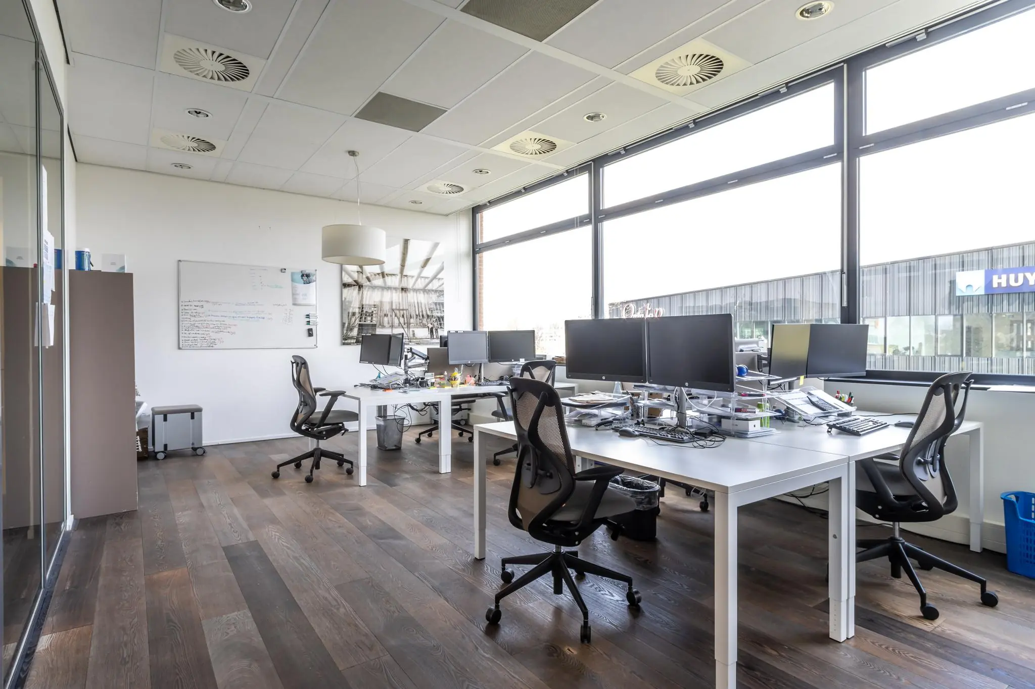 Moderne kantoorruimte aan de Groenewoudsedijk met meerdere bureaus, beeldschermen en ergonomische stoelen bij grote ramen.