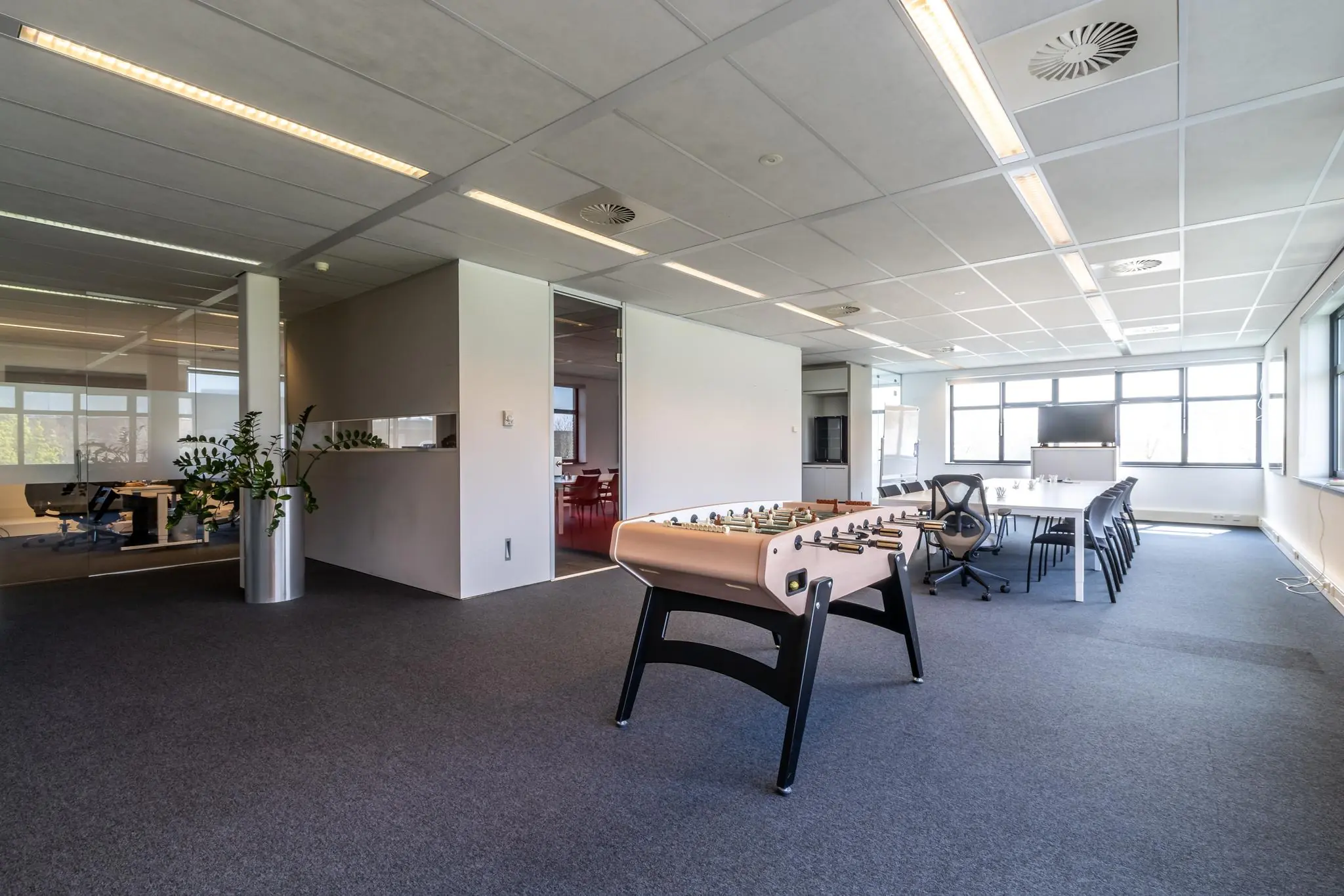 Moderne kantoorruimte aan de Groenewoudsedijk met vergadertafel, tafelvoetbaltafel en glazen wanden.
