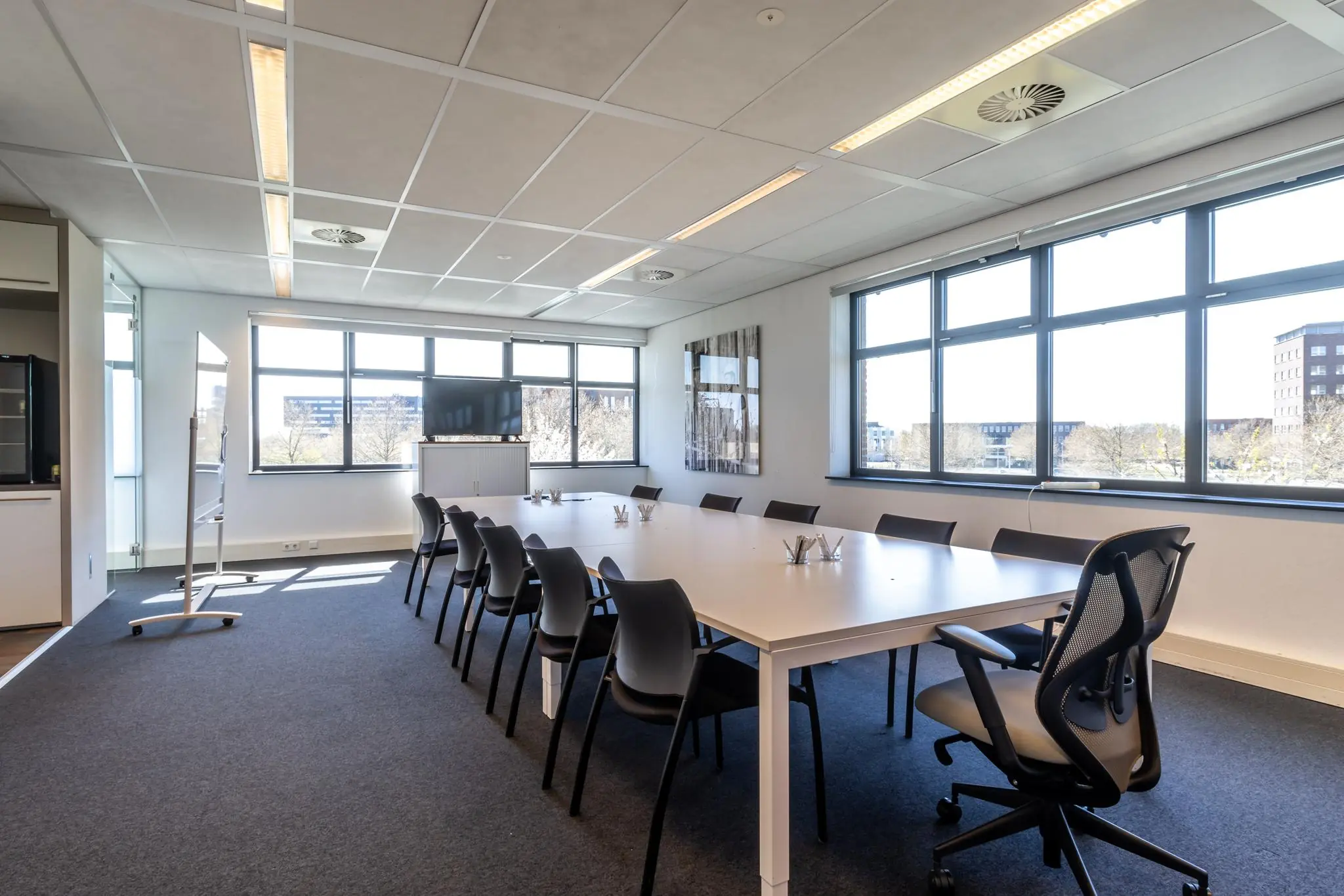 Vergaderruimte aan de Groenewoudsedijk met een lange tafel, bureaustoelen, groot raam en presentatiescherm.