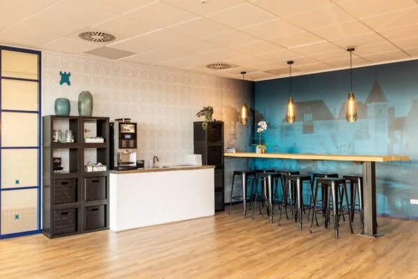 Moderne bedrijfskeuken met koffieautomaat, houten vloer en hoge zitplaatsen aan een bar met sfeerverlichting.