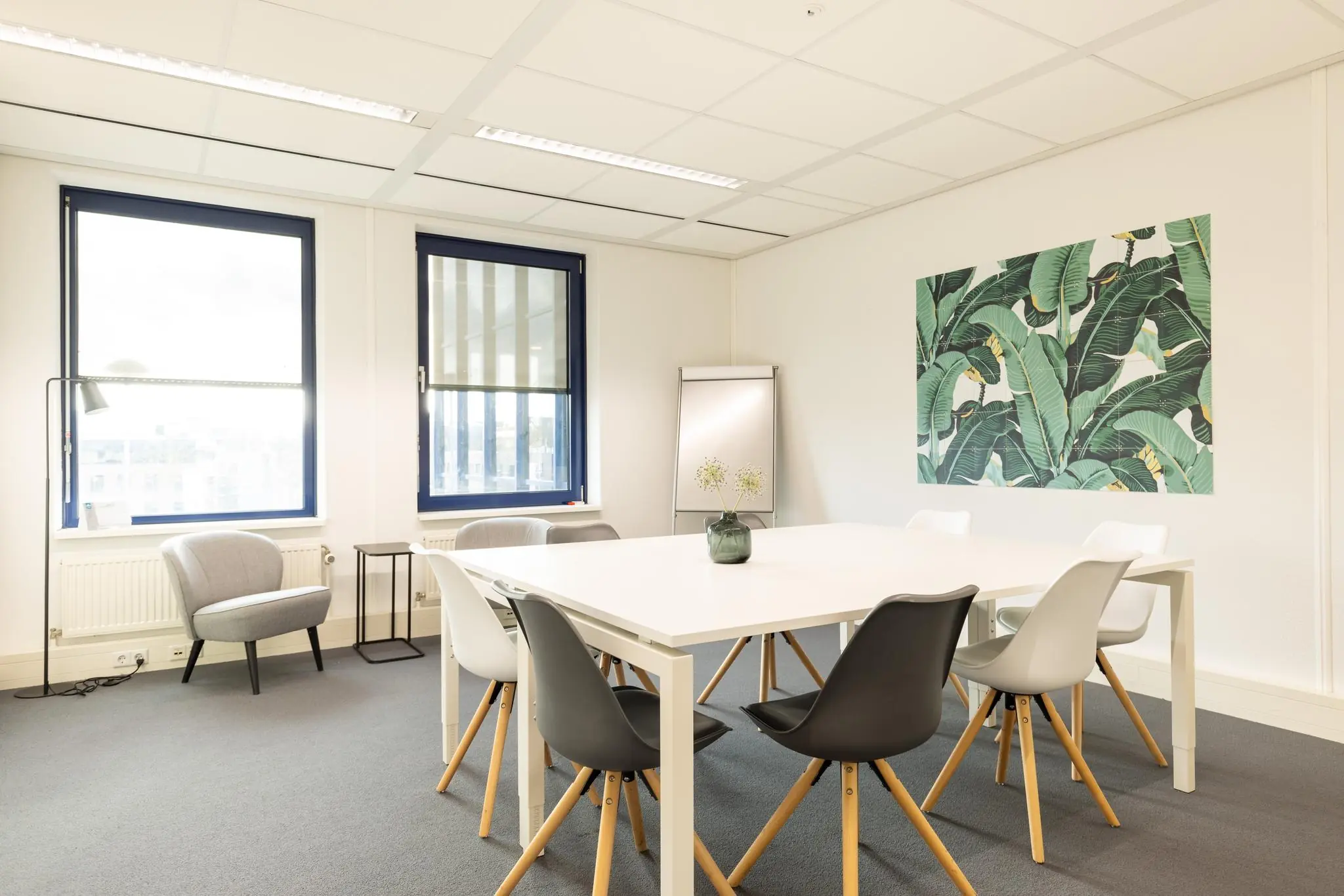 Vergaderruimte aan de Fokkerstraat met moderne meubels, grote ramen en een wanddecoratie met groene bladeren.