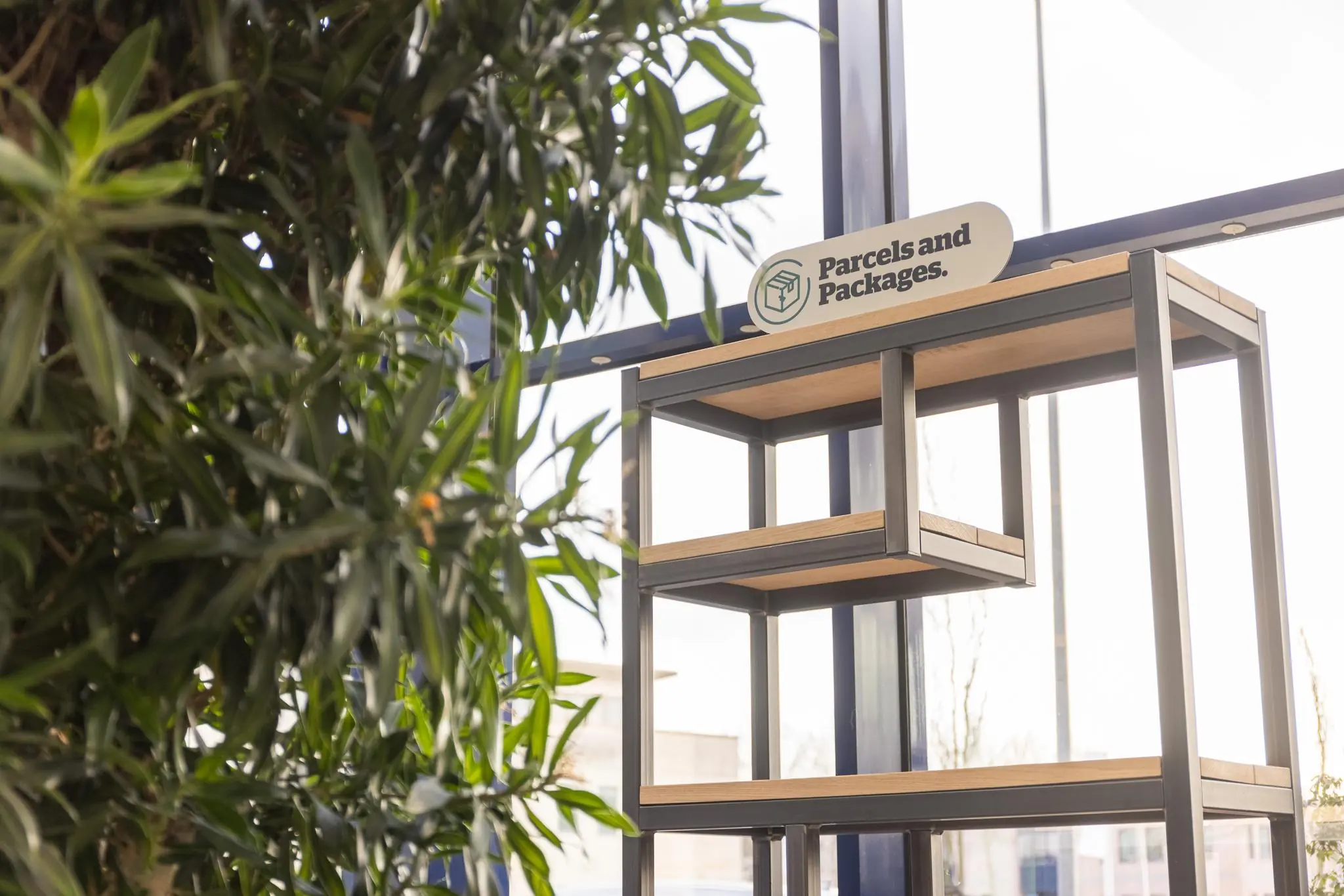 Open stellingkast met houten legplanken en het bord “Parcels and Packages” in een lichte, groene binnentuinruimte aan de Fokkerstraat.
