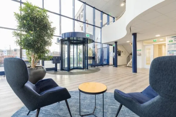 Moderne en lichte entreehal aan de Fokkerstraat met zitgelegenheid, een grote plantenbak en een glazen draaideur.