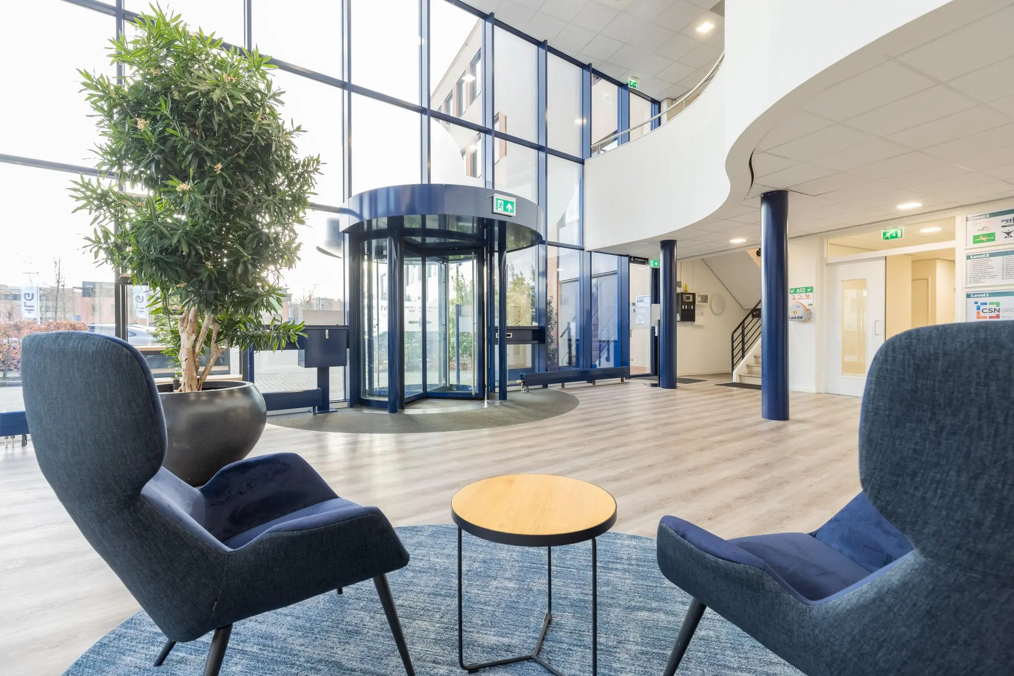 Moderne en lichte entreehal aan de Fokkerstraat met zitgelegenheid, een grote plantenbak en een glazen draaideur.