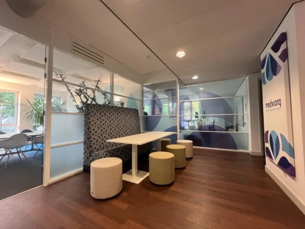 Moderne kantoorruimte aan de Driebergseweg met een zitje, glazen wanden en het logo van Medworq op de muur.