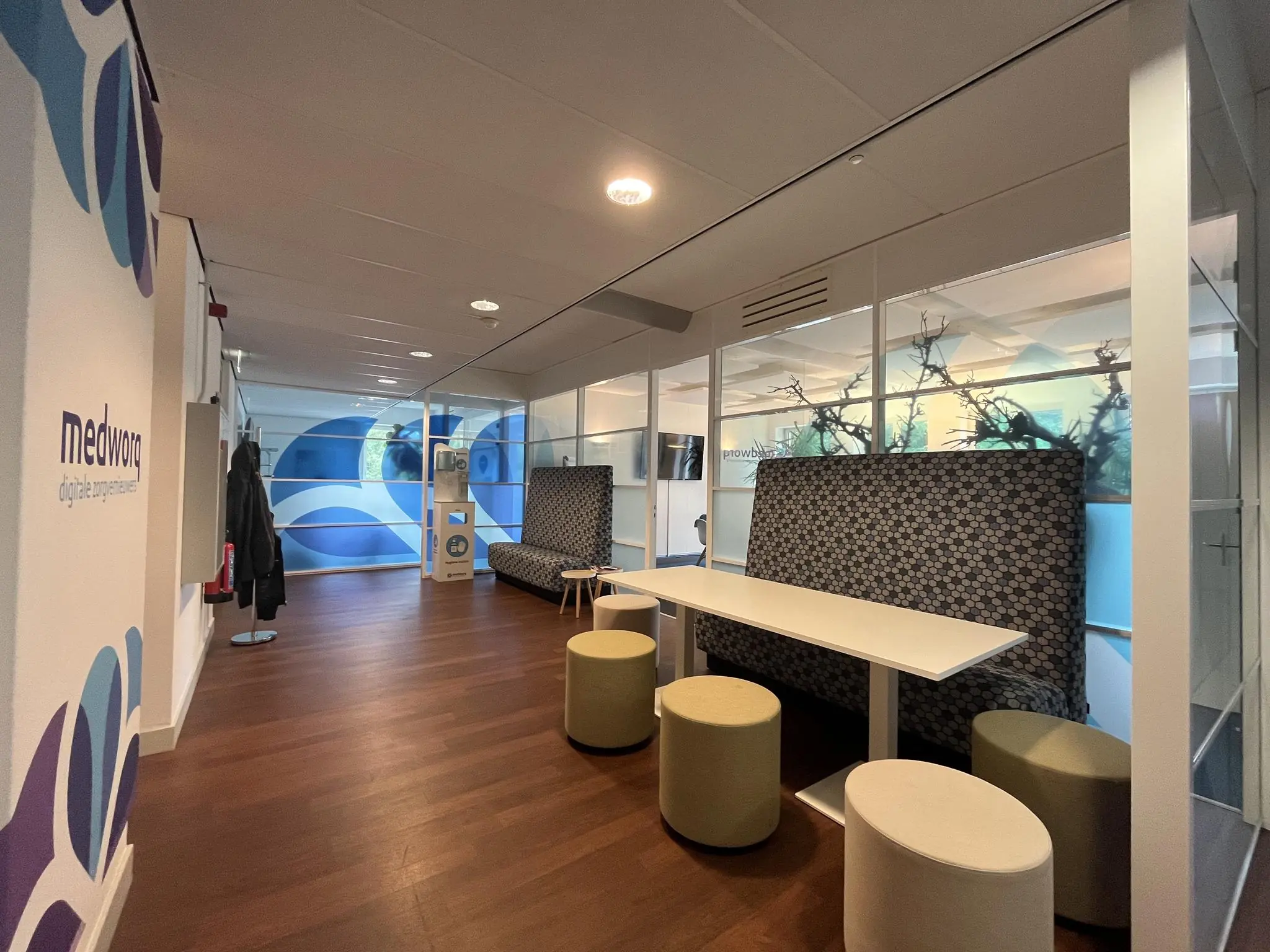 Moderne kantoorruimte bij Medworq aan de Driebergseweg met zithoek, glazen wanden en kleurrijke wanddecoratie.