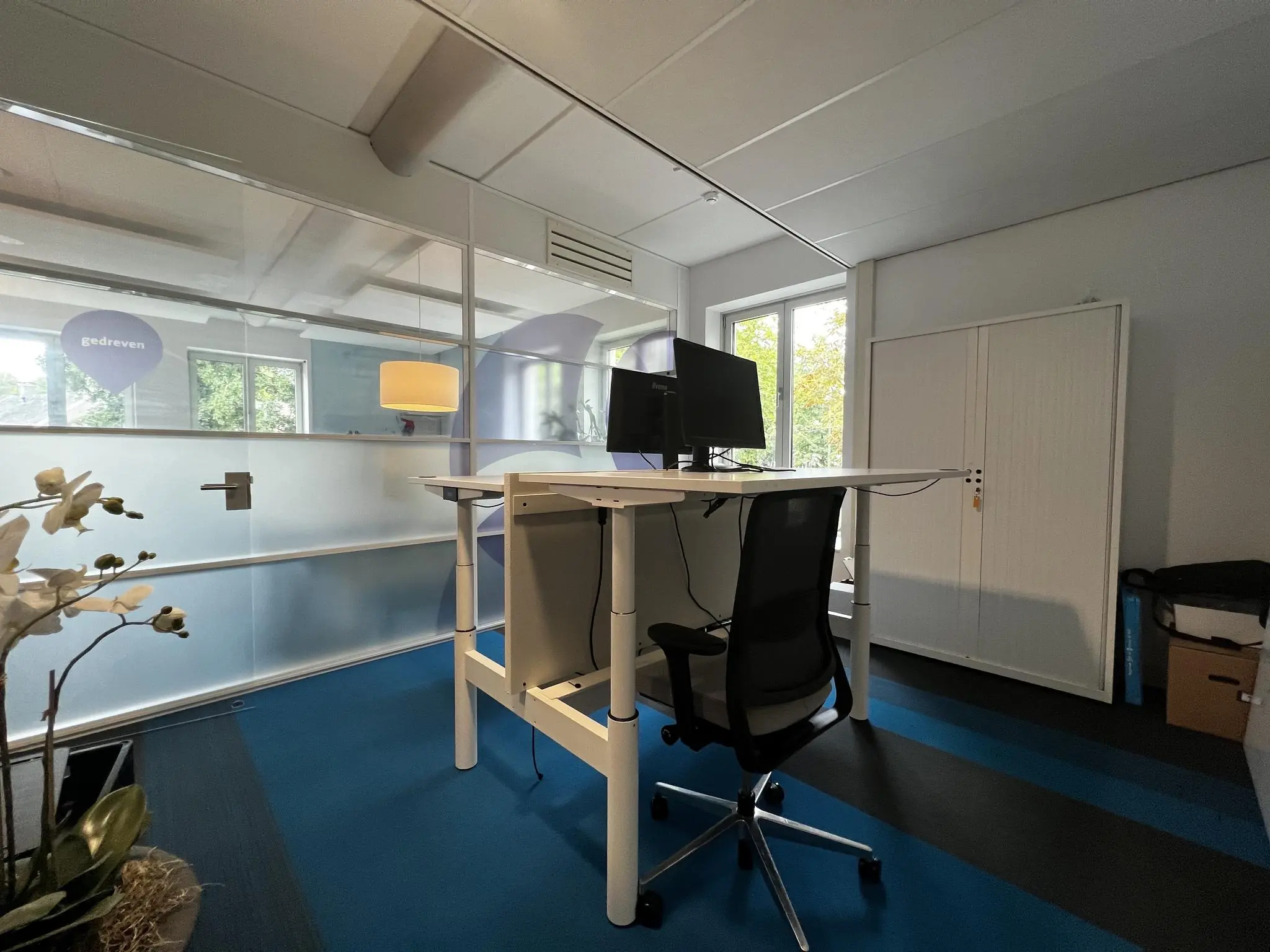 Modern ingericht kantoor met zit-sta bureau, bureaustoel en glazen scheidingswand op de Driebergseweg.