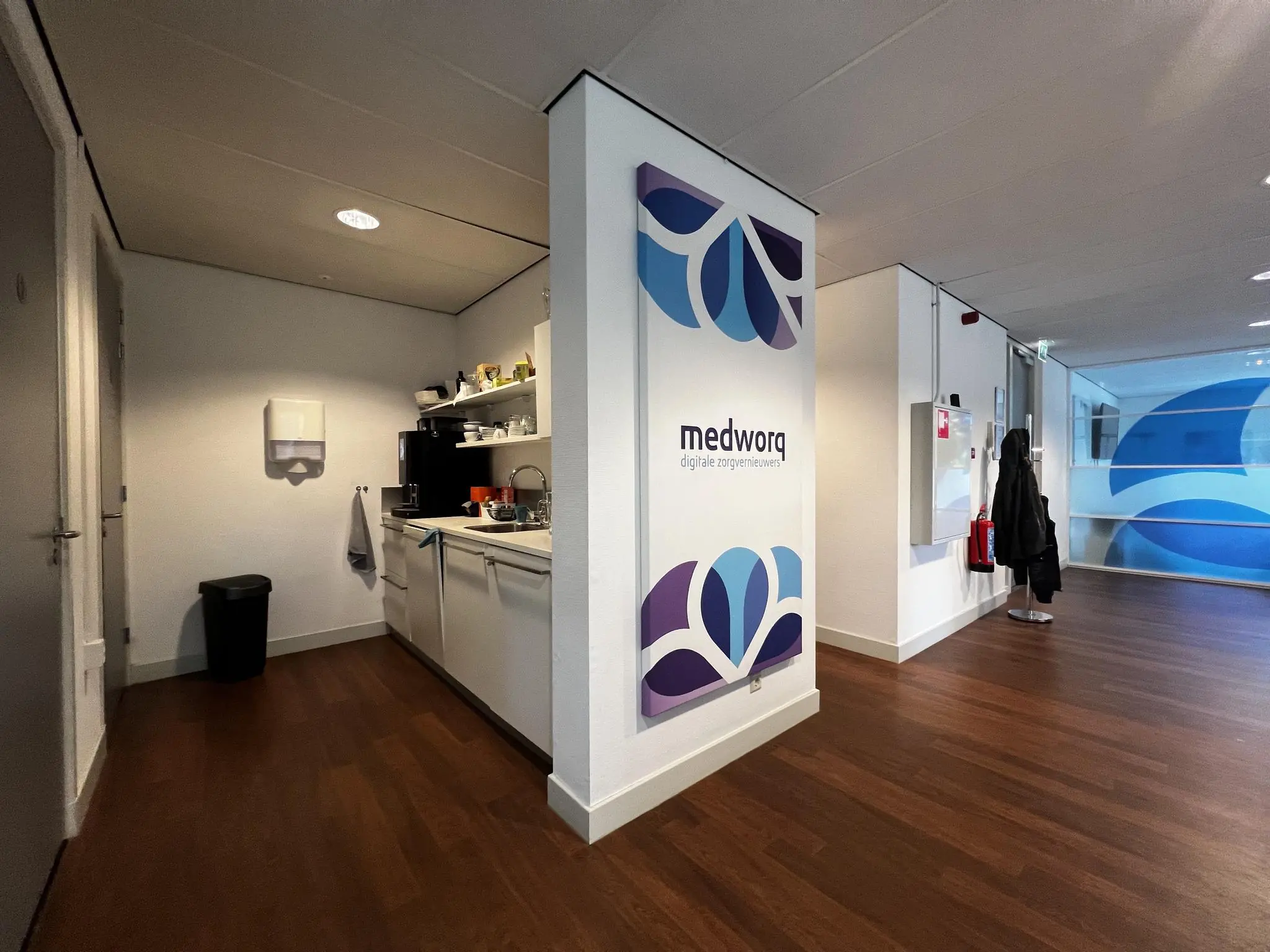 Kleine kantoorkeuken en gang met zicht op het logo en de naam van Medworq aan de Driebergseweg.