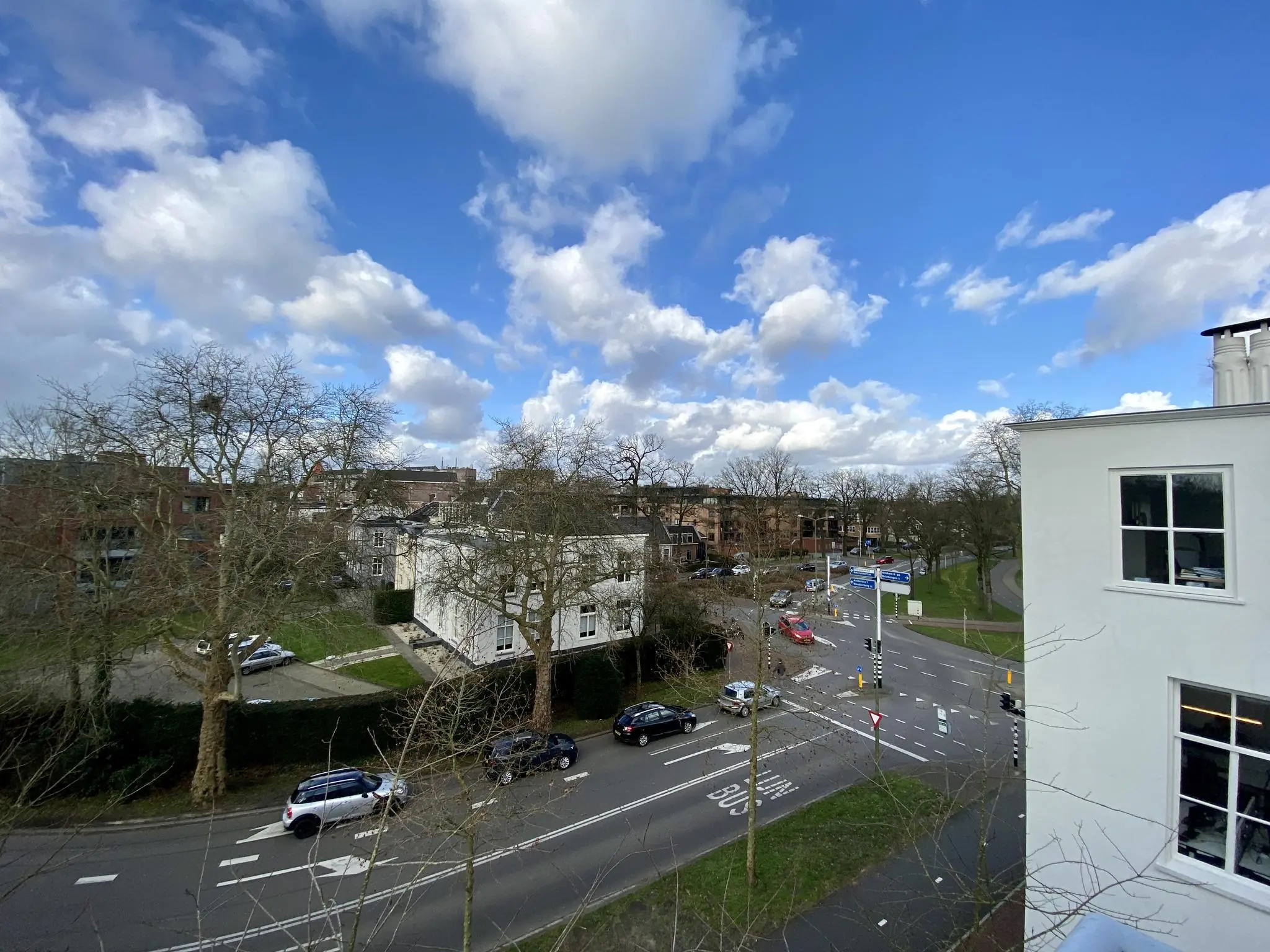 Kruispunt op de Driebergseweg in een stadsomgeving met auto’s, gebouwen en deels bewolkte blauwe lucht.