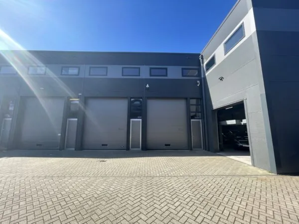 Moderne bedrijfsunits aan de Aalsmeerderweg met gesloten en deels geopende roldeuren onder een strakblauwe lucht.
