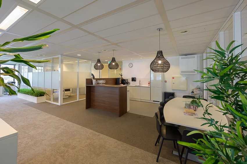 Moderne kantoorruimte aan de Bahialaan met een open keuken, vergadertafel en veel groenaccenten.