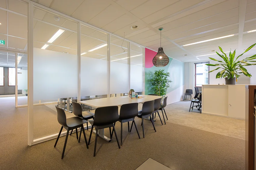 Moderne vergaderruimte aan de Bahialaan met glazen wanden, zwarte stoelen en planten voor een frisse uitstraling.