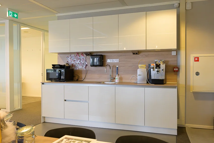 Moderne kantoorpantry aan de Bahialaan met witte kasten, koffieapparaat, magnetron en spoelbak.