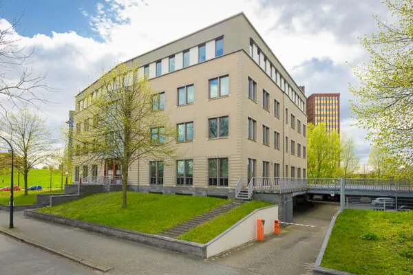 Kantoorgebouw aan de Bahialaan met beige gevel en oprijlaan naar parkeergarage, omringd door bomen en groen.