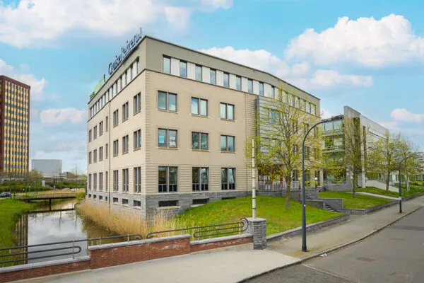 Modern kantoorgebouw aan de Bahialaan met het logo van CruiseReizen op het dak, gelegen naast een waterpartij en omgeven door bomen.