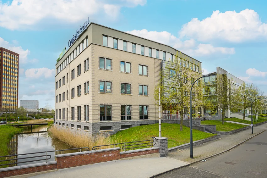 Modern kantoorgebouw aan de Bahialaan met het logo van CruiseReizen op het dak, gelegen naast een waterpartij en omgeven door bomen.