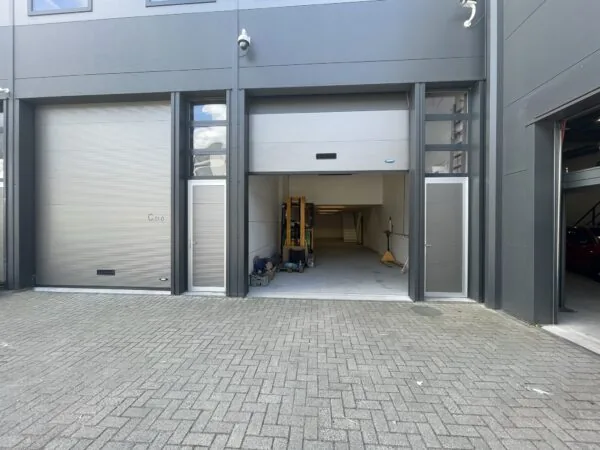 Bedrijfsunit aan de Aalsmeerderweg met openstaande overheaddeur en zicht op het interieur met heftruck en trap.