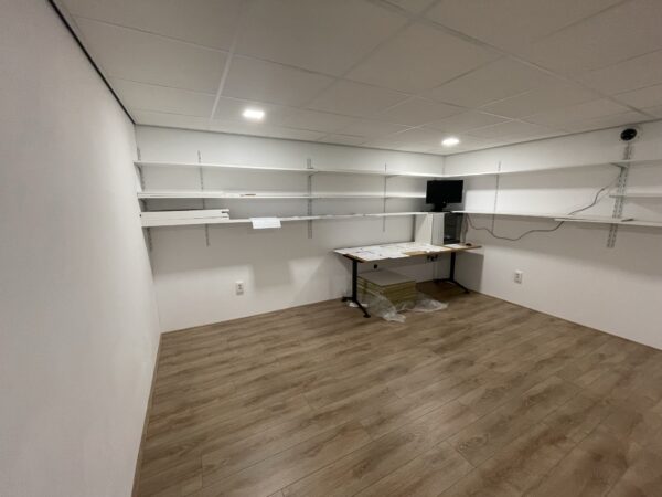 Kleine, lege opslag- of werkruimte aan de Aalsmeerderweg met witte wandplanken, een houten vloer en een bureau met computer.