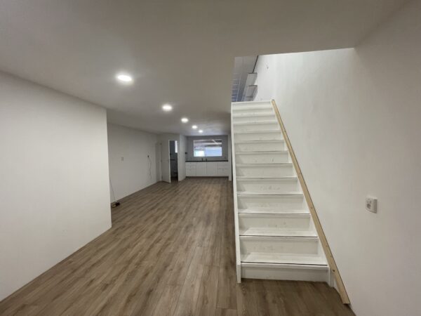 Een moderne, gerenoveerde ruimte aan de Aalsmeerderweg met houten vloer, witte trap en open keuken achterin.