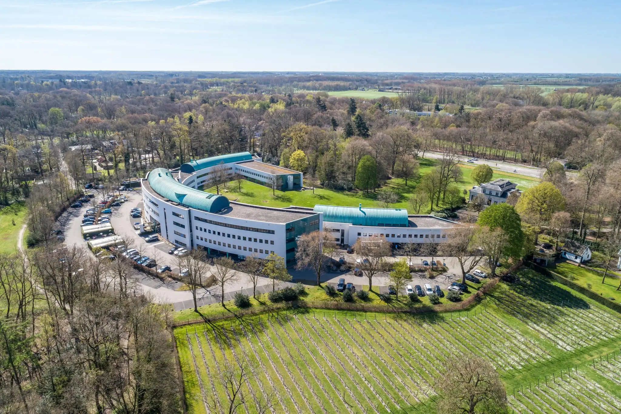 Luchtfoto van het moderne gebouw Sparrenheuvel, gelegen tussen bos en weilanden.