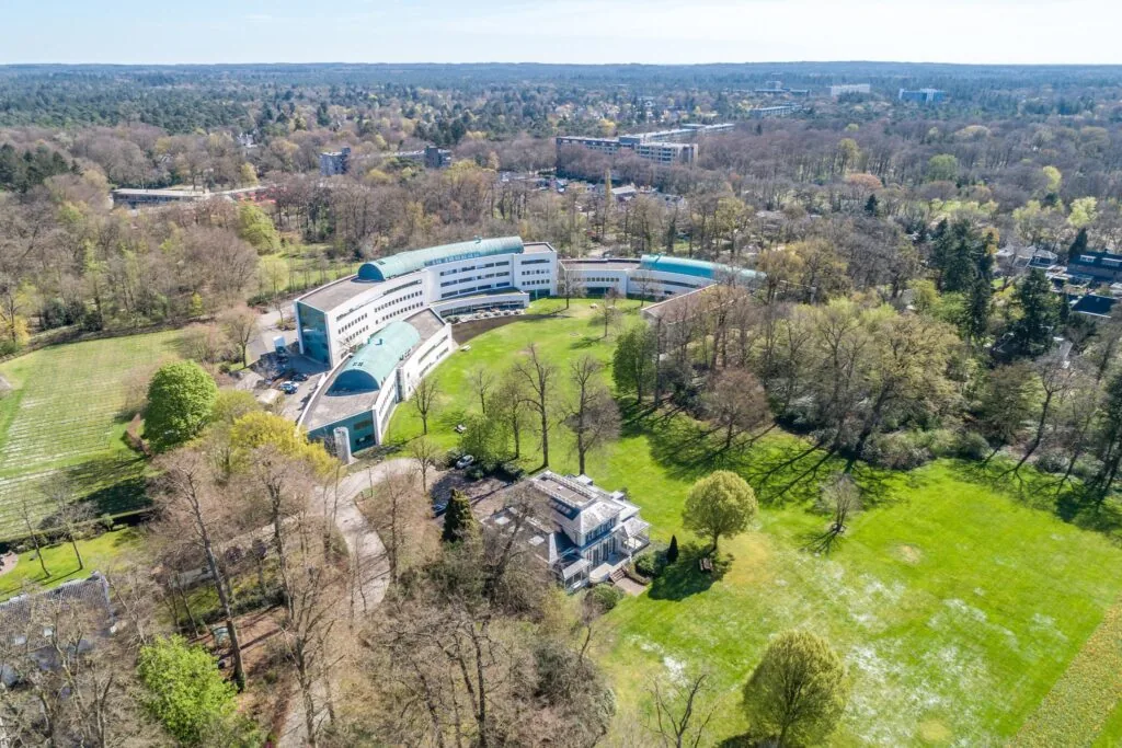 Luchtfoto van het kantoorgebouw Sparrenheuvel in een bosrijke omgeving met grasvelden en bomen.