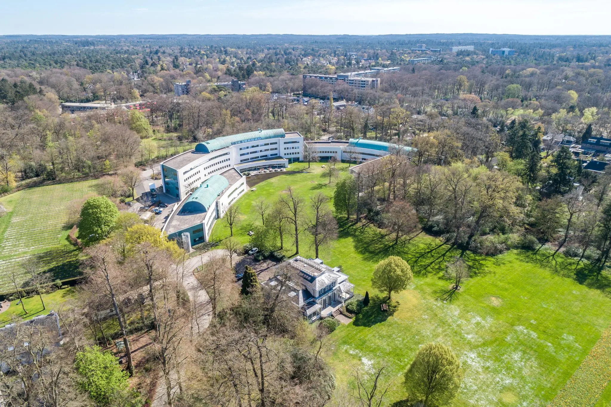 Luchtfoto van het kantoorgebouw Sparrenheuvel in een bosrijke omgeving met grasvelden en bomen.