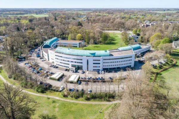Luchtfoto van het witte gebouw van Kliniek Sparrenheuvel, omgeven door bomen en parkeerplaatsen.