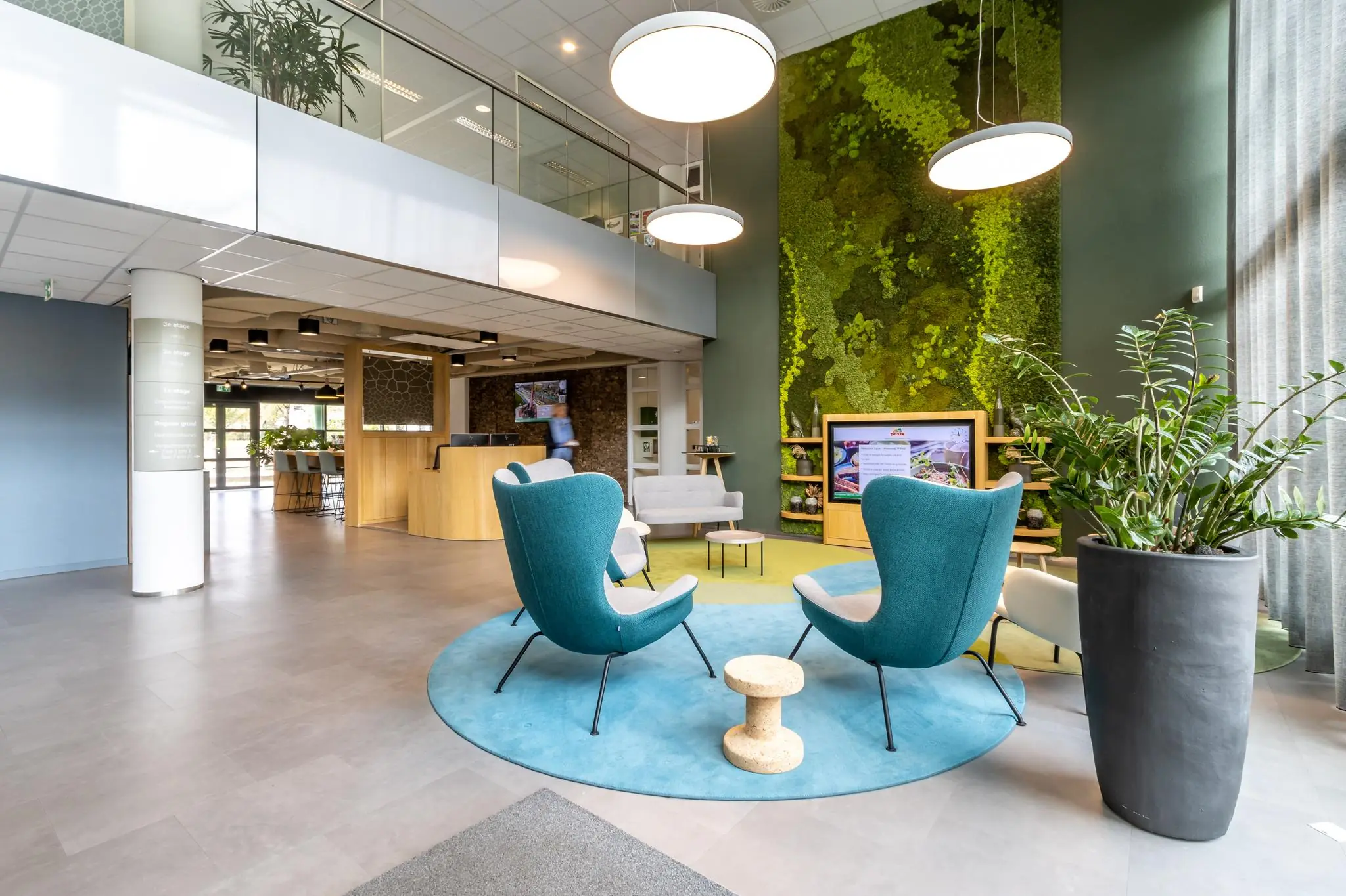 Moderne en lichte wachtruimte in gezondheidscentrum Sparrenheuvel met groene moswand, designmeubels en een informatiescherm.