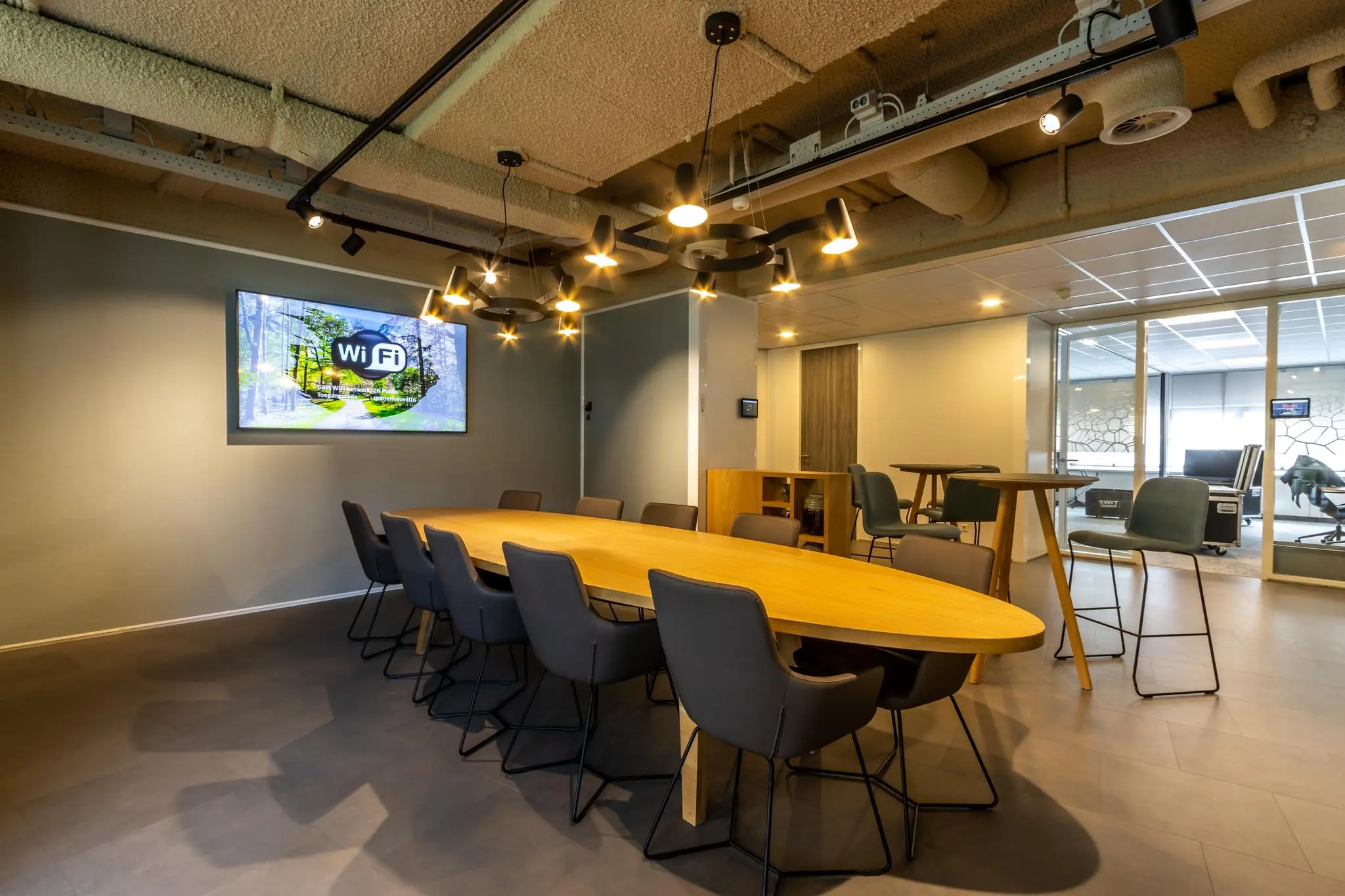 Vergaderruimte Sparrenheuvel met een lange houten tafel, moderne stoelen en een scherm aan de muur.