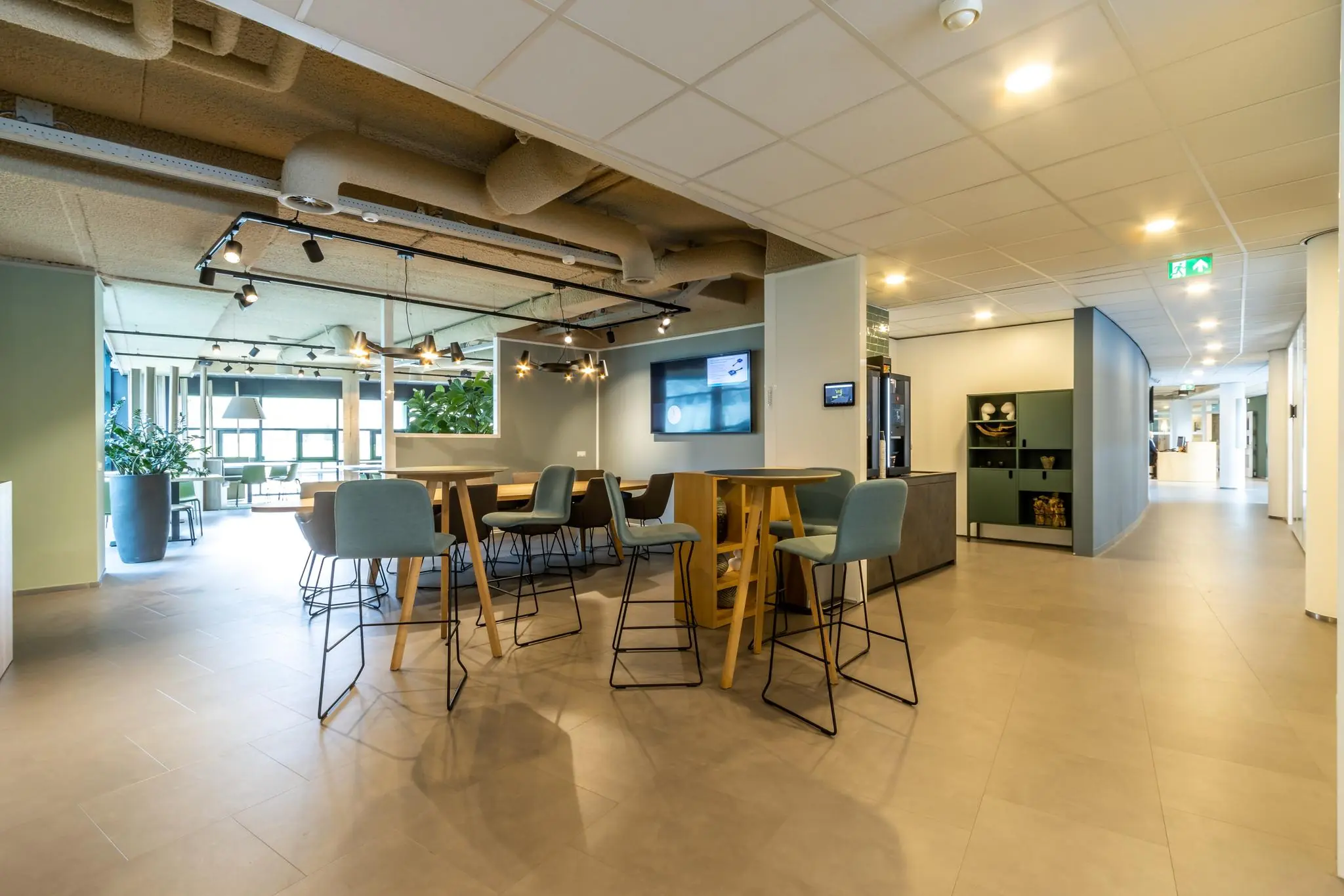 Moderne kantoorruimte in Sparrenheuvel met hoge tafels, barkrukken, planten en sfeervolle verlichting.