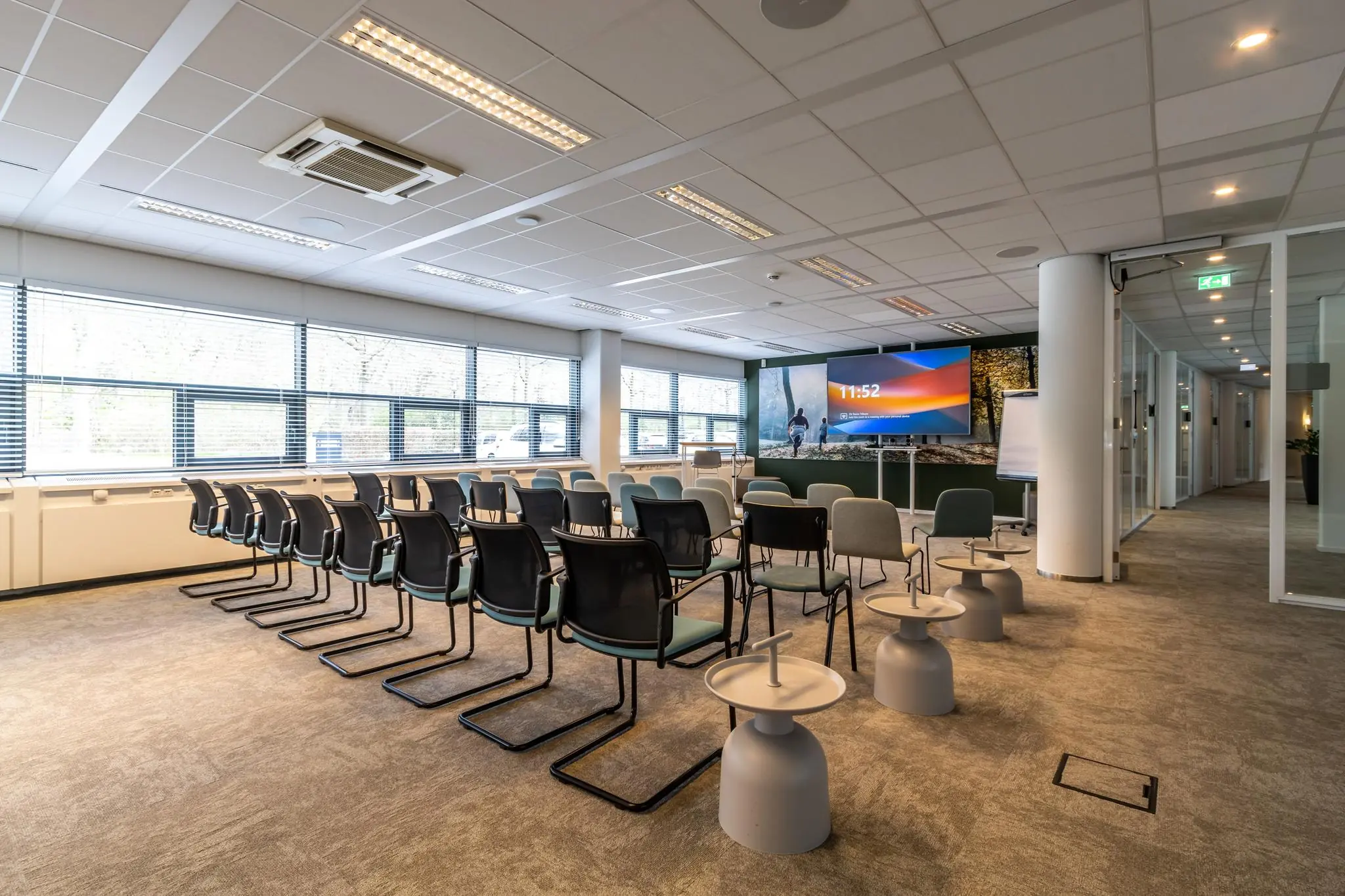 Moderne vergaderruimte in Sparrenheuvel met opstellingen van stoelen, bijzettafeltjes en een groot presentatiescherm.