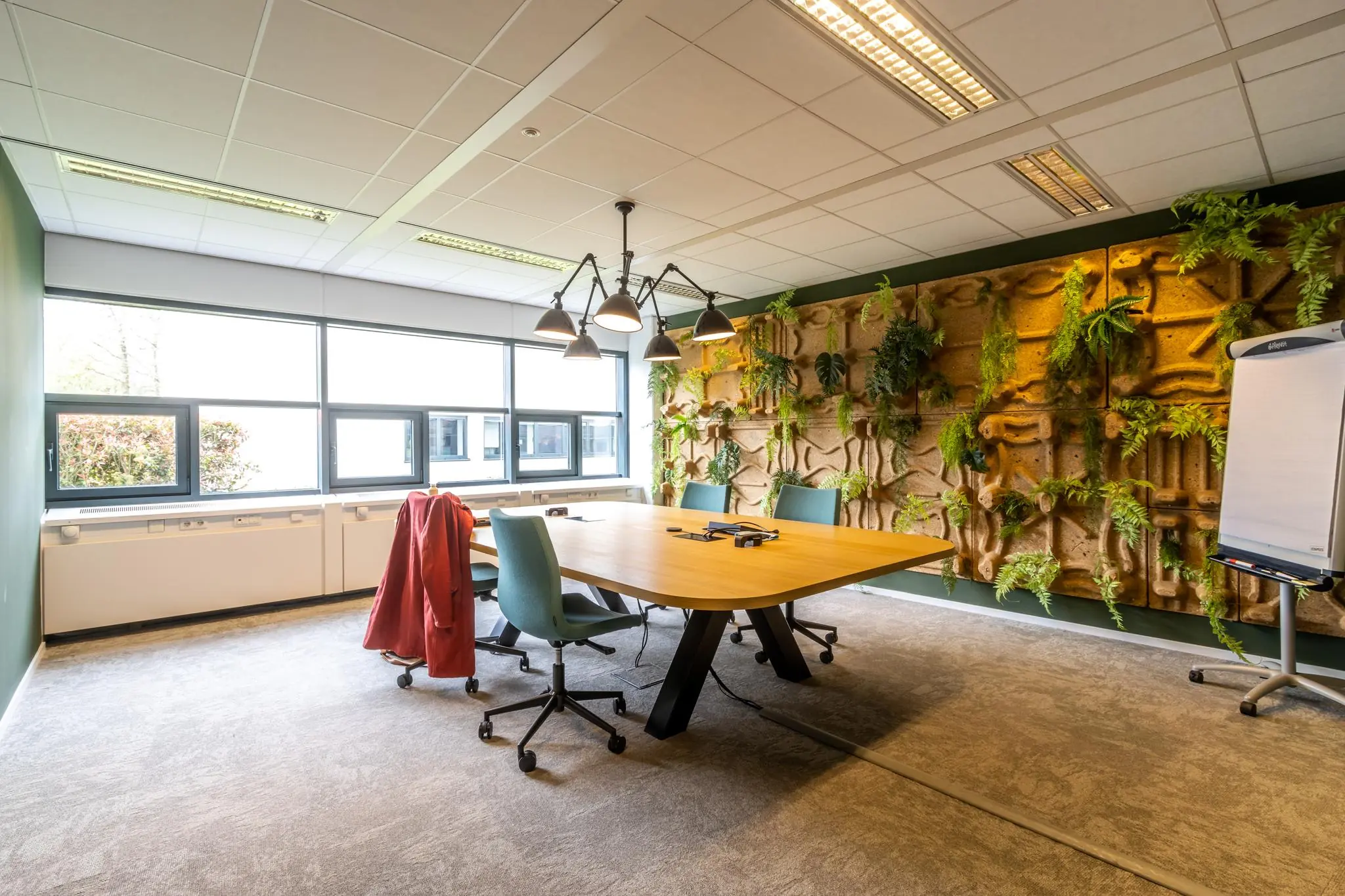Vergaderruimte Sparrenheuvel met houten tafel, groene stoelen, een moswand en veel natuurlijk licht.