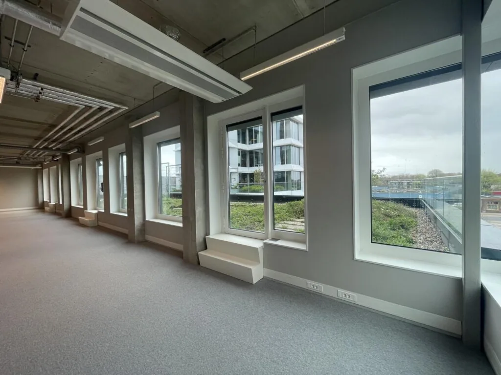 Lichte, lege kantoorruimte aan de Asterweg met grote ramen en uitzicht op een modern kantoorgebouw.