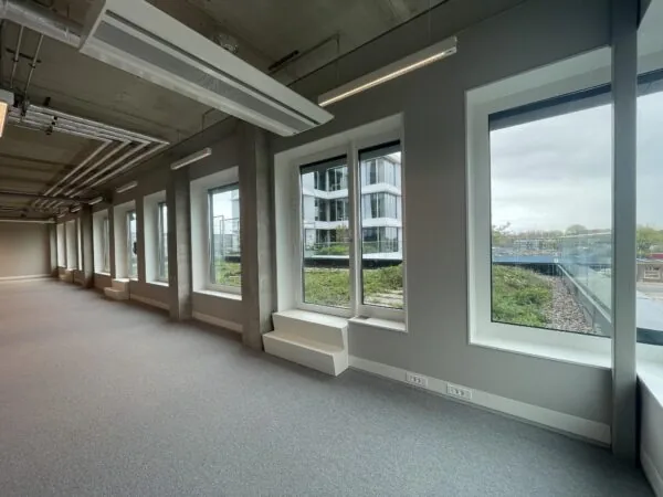 Lichte, lege kantoorruimte aan de Asterweg met grote ramen en uitzicht op een modern kantoorgebouw.