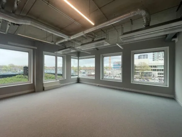 Lichte, leegstaande kantoorruimte aan de Asterweg met grote ramen en zicht op een stedelijke omgeving.